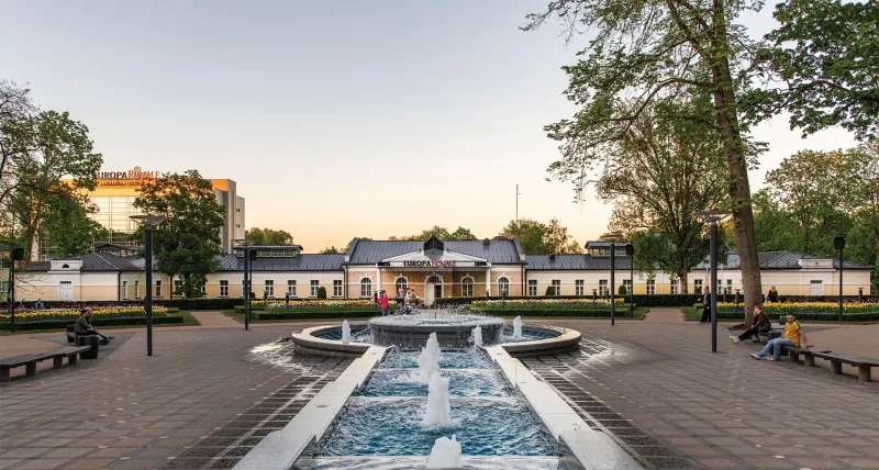 Fountain and tree-lined promenade in front of Europa Royale Druskininkai at dusk