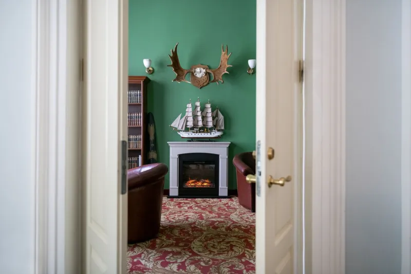 Lounge with green walls, a fireplace and a model sailing ship on the mantel