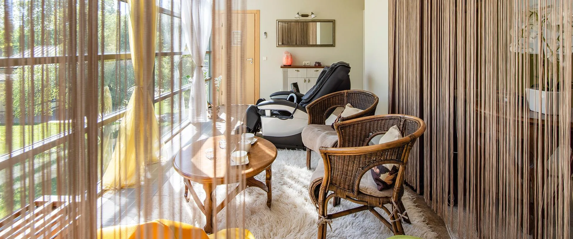 Relaxation room with rattan chairs and sheer curtains along a glazed wall