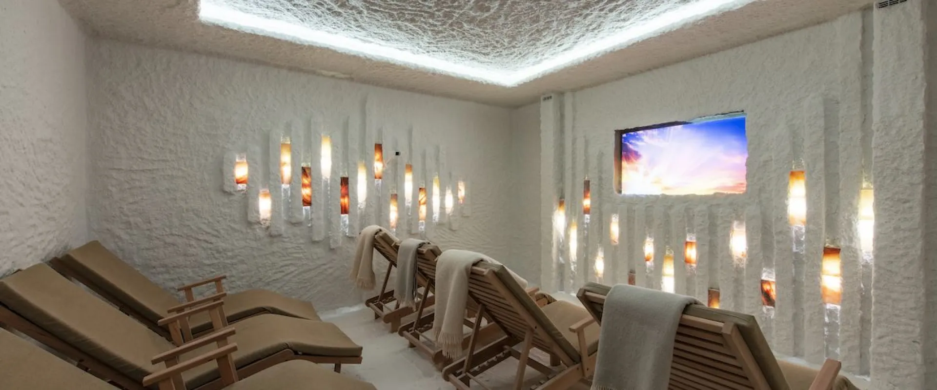 Salt room with wooden loungers, a textured backlit ceiling and glowing salt panels on the walls