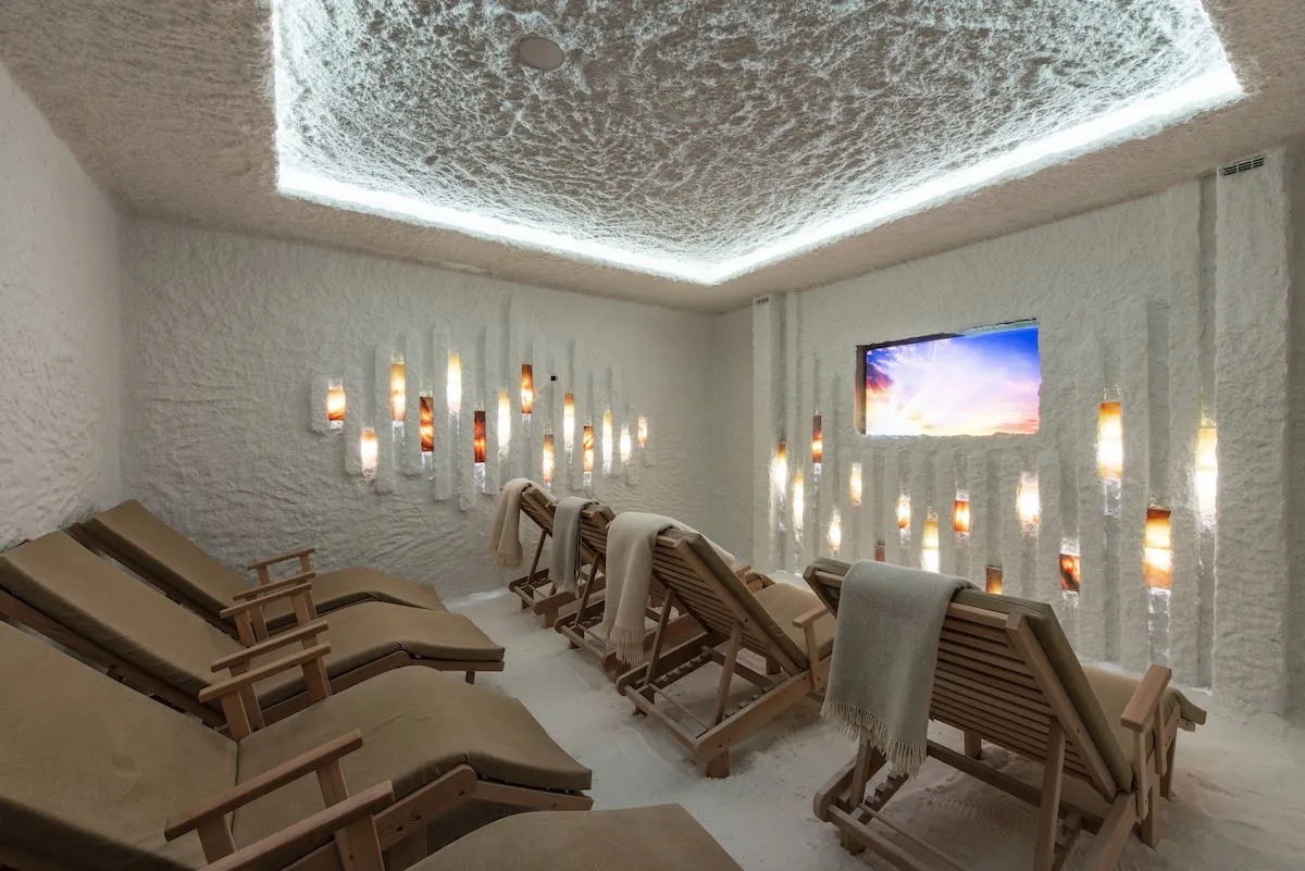 Salt room with wooden loungers, a textured backlit ceiling and glowing salt panels on the walls