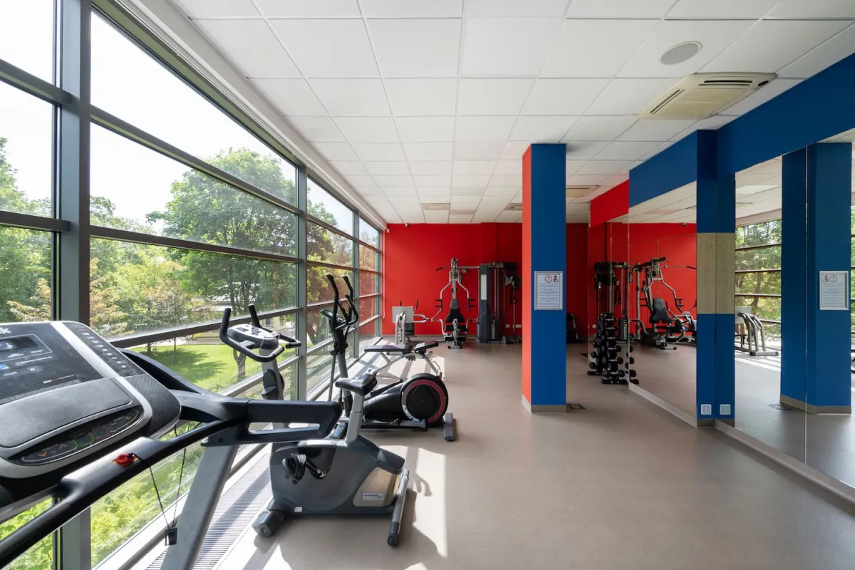 Gym with treadmills and exercise bikes along a glass wall and weight machines by a red wall