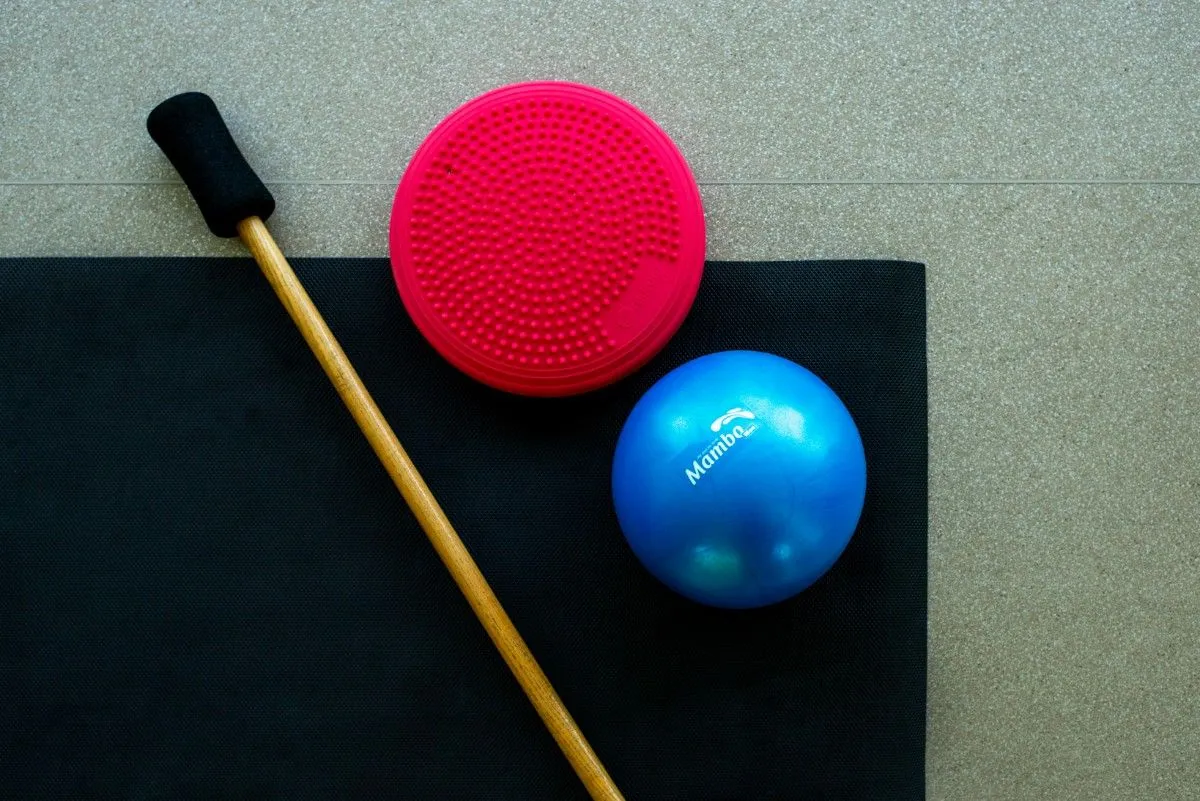 Red balance cushion, blue exercise ball and a wooden gymnastic stick on a black mat