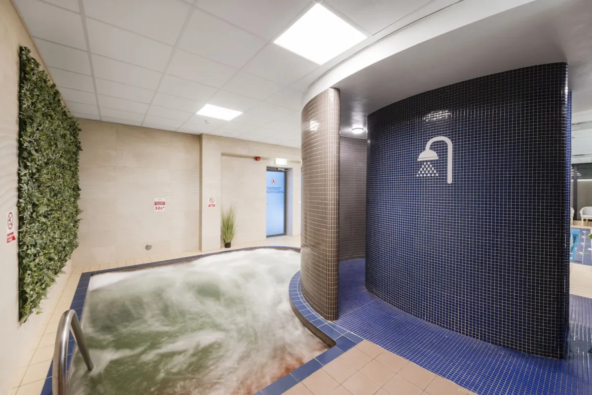 Whirlpool bath beside a dark mosaic-tiled shower column and a green plant wall