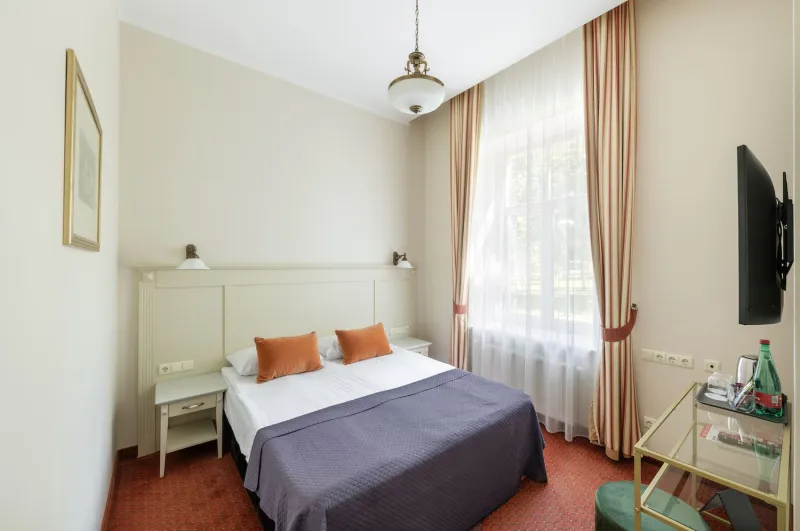 Guest room with a double bed, pendant lamp, curtained window, wall-mounted TV and a drinks trolley