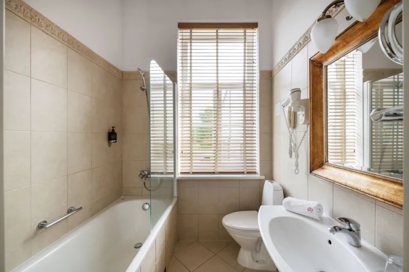 Bathroom with a bath and glass screen under a shuttered window, toilet and basin by a wooden-framed mirror