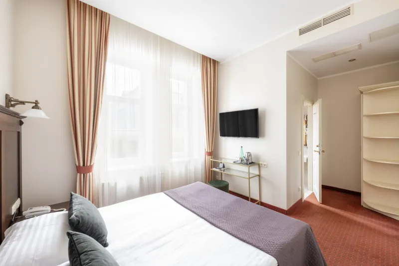 Guest room with a double bed, wall-mounted TV, small desk and curved white corner shelving