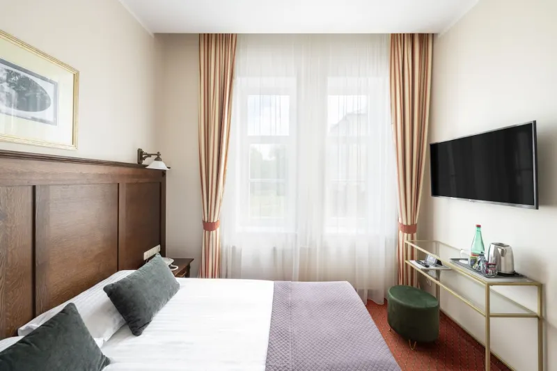 Guest room with a wooden-headboard bed, curtained windows, wall-mounted TV and a desk with a green stool