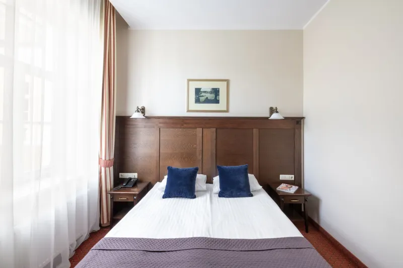 Hotel bed with two navy cushions against a tall wood-panelled headboard, framed print above