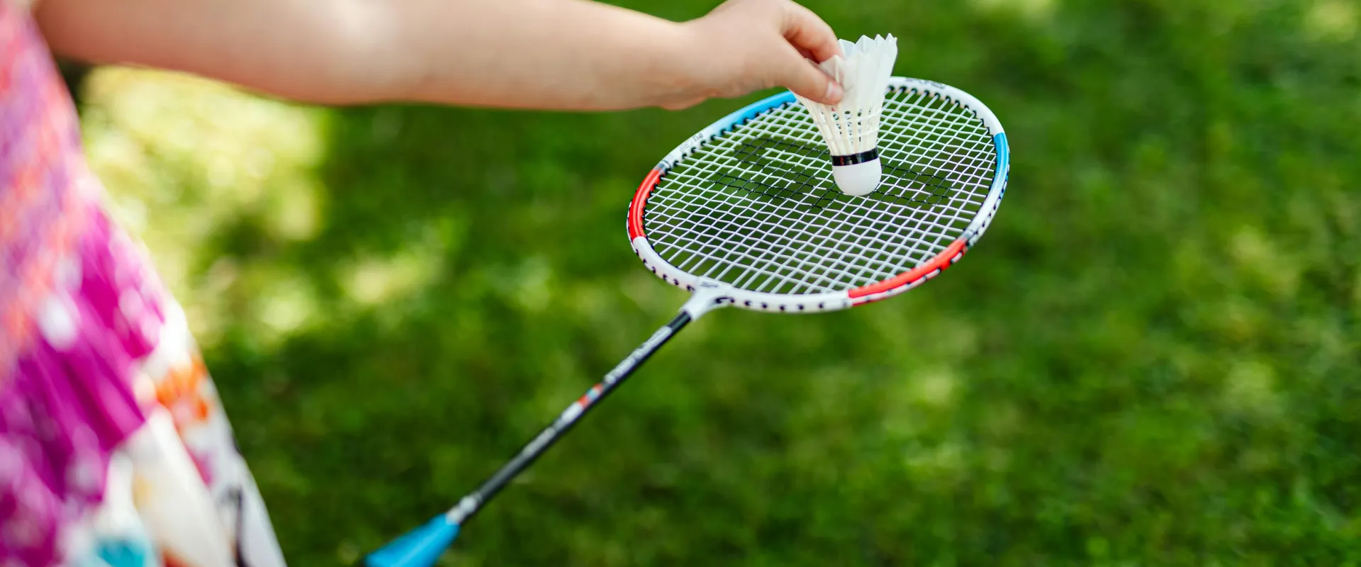 Child holding a badminton racket and shuttlecock on a lawn