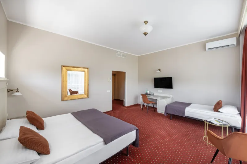 Spacious room with a double bed, an extra single bed, a desk with a TV and a gold-framed mirror