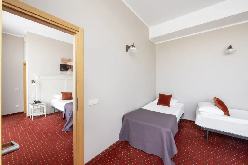 Two adjoining rooms with single beds seen through an open connecting doorway