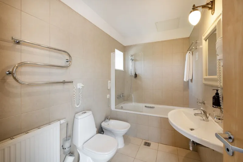 Bathroom with a curved chrome towel radiator, bathtub, toilet and washbasin under beige tiling