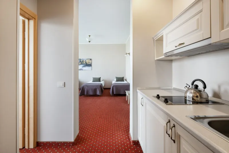 Kitchenette with a kettle and hob in the foreground, looking down a corridor to two single beds