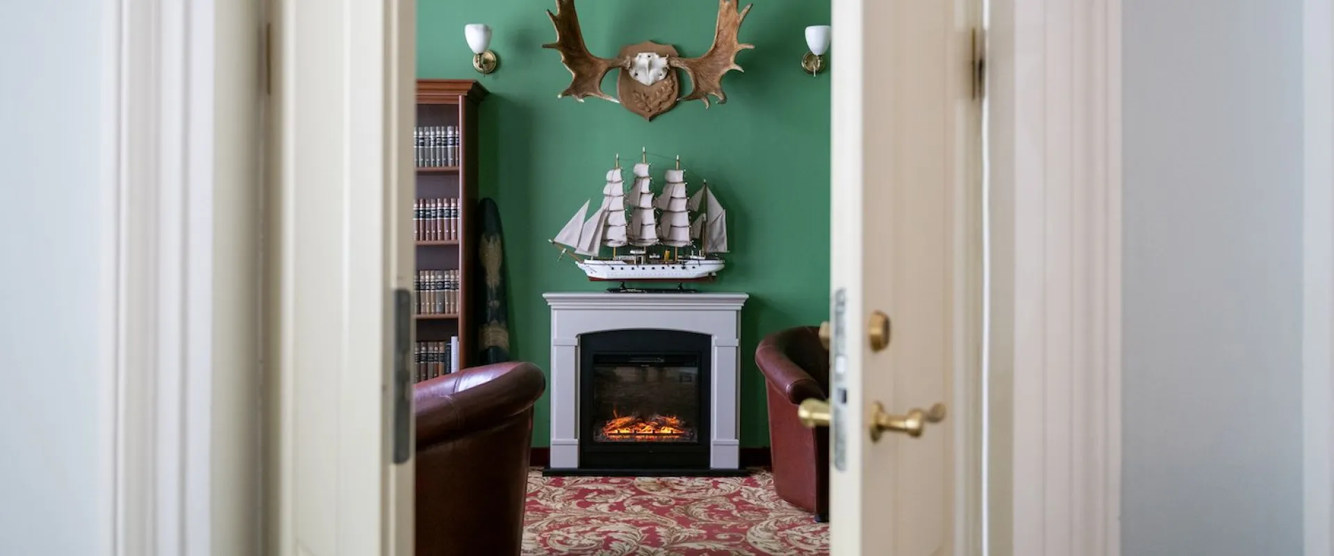 Lounge with green walls, a fireplace and a model sailing ship on the mantel