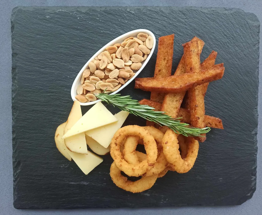 Slate board of snacks: fried bread sticks, onion rings, cheese slices, peanuts and a rosemary sprig