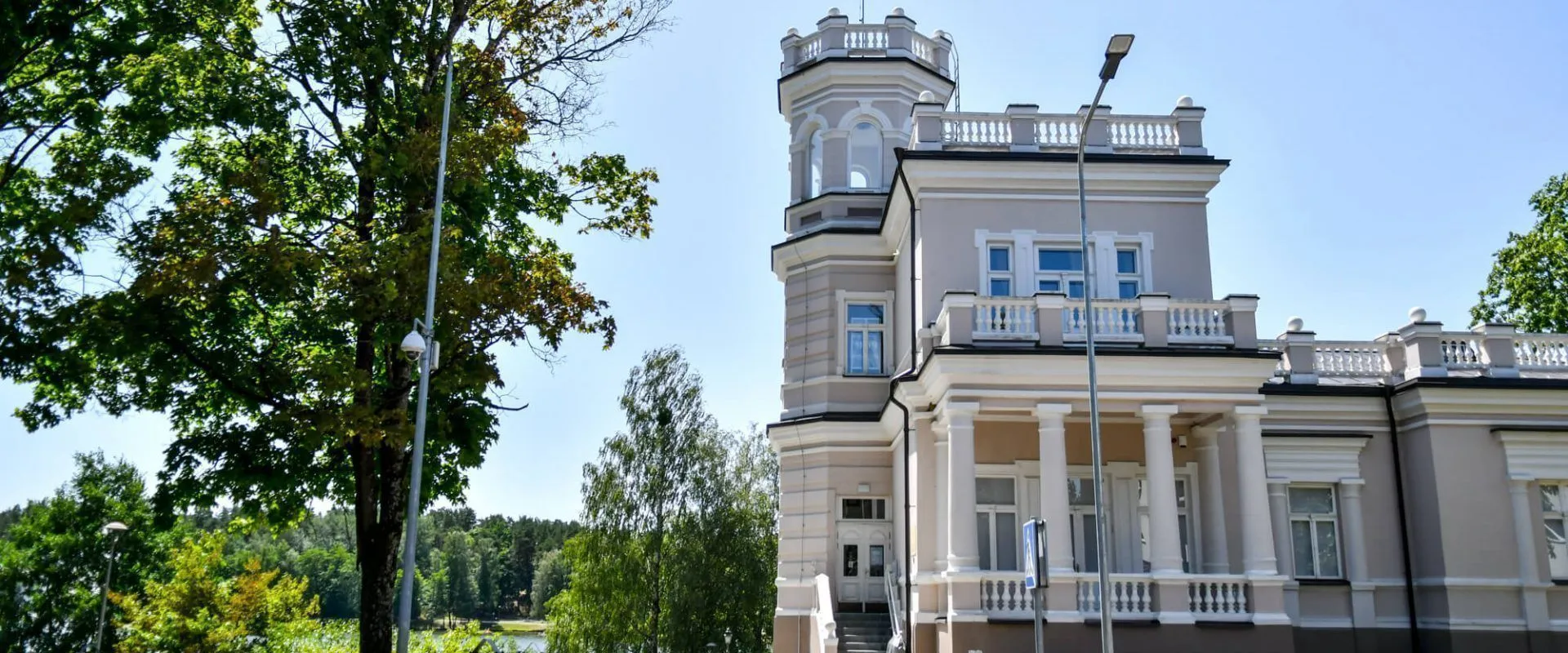 White manor-style spa building with a turret behind summer trees