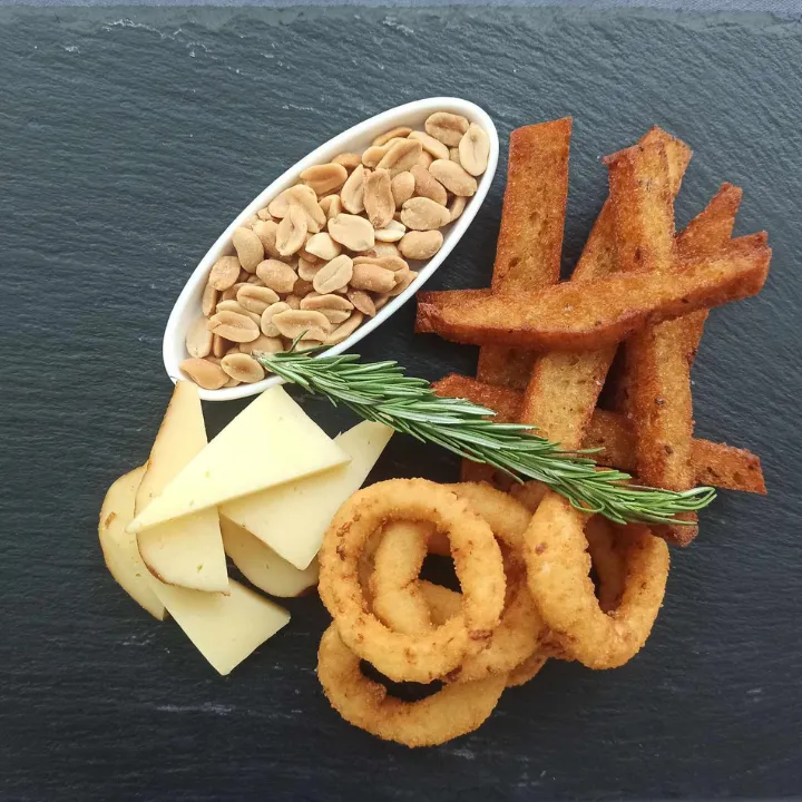 Slate board with cheese, bread sticks, onion rings and nuts