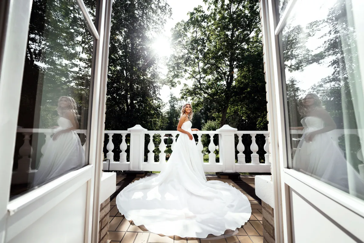 Bride in a long gown on a balcony framed by tall windows